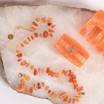 Sui Ava Halskjede Amber med stener i ulike oransje farger og justerbar lås i messing, vist sammen med Sui Ava Hårklype Fie Apricot